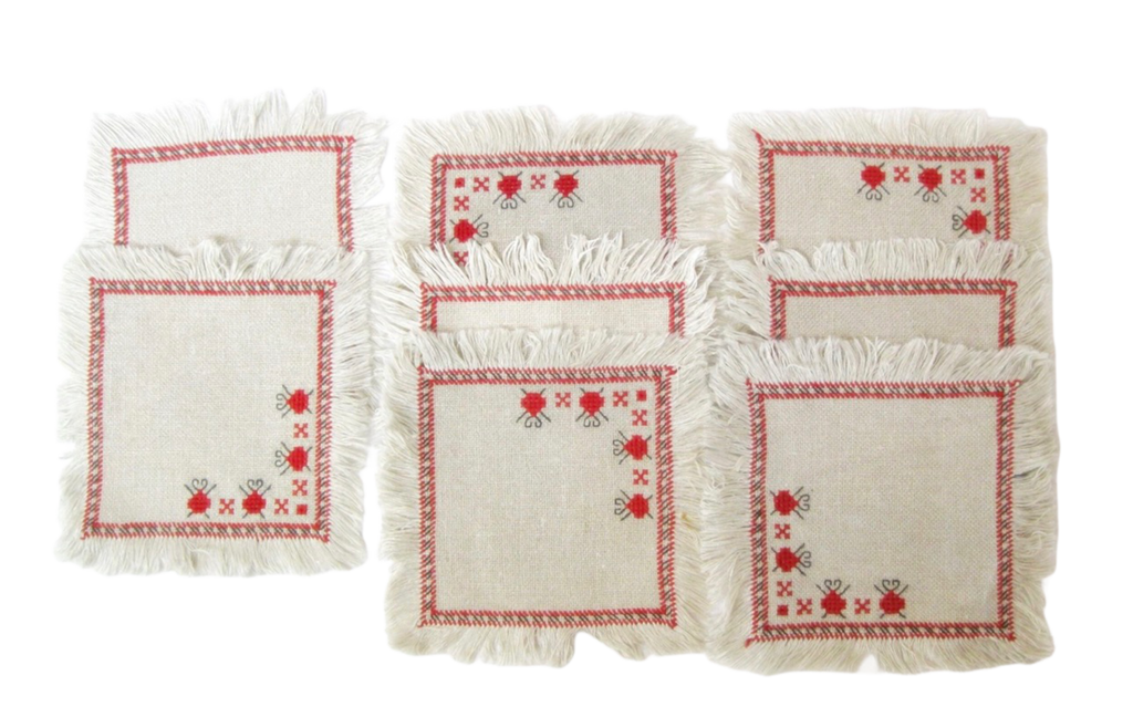 Set of four embroidered placemats with red patterns on a white background