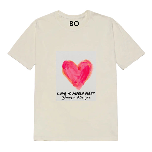 A organic cotton t-shirt with a front print of a red heart and the phrase 'Love Yourself First' on it. Love Yourself First tee — white organic cotton t-shirt with love print, unisex fit, mental health charity tee