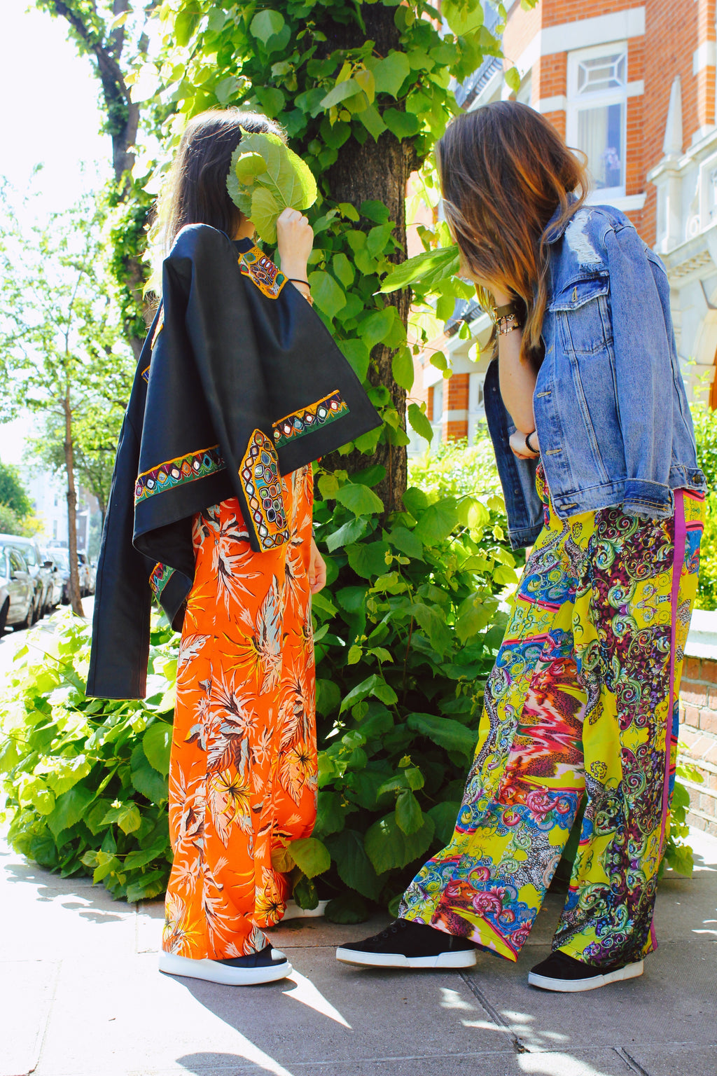 Two people in colorful outfits standing outdoors next to a tree. Yellow patterned silk pants — handmade yellow silk designer pants with groovy print from Hanout Boutique Marrakech, relaxed fit