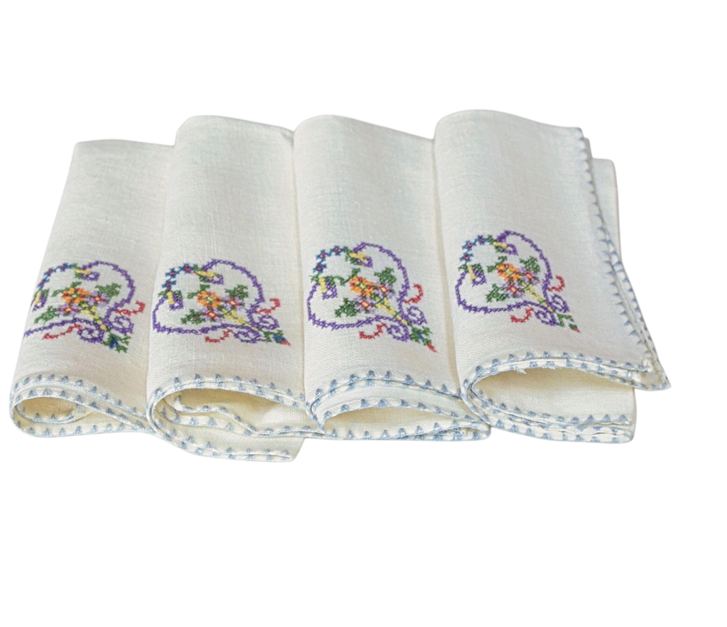 Set of four folded white napkins with embroidered designs on a white background