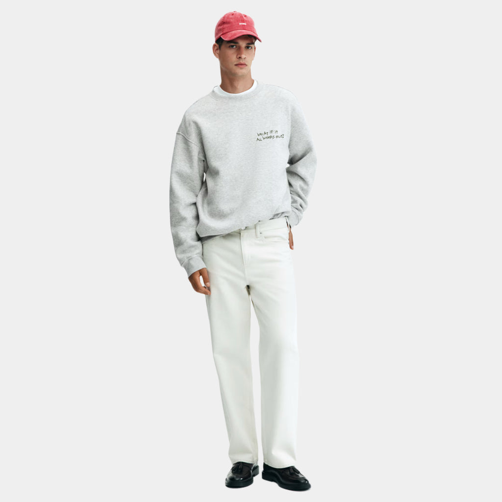 Person wearing a gray sweatshirt, white pants, and a red cap on a white background. It Will All Work Out sweatshirt — grey 320gsm organic cotton charity sweatshirt, unisex fit, multi-cause made-to-order