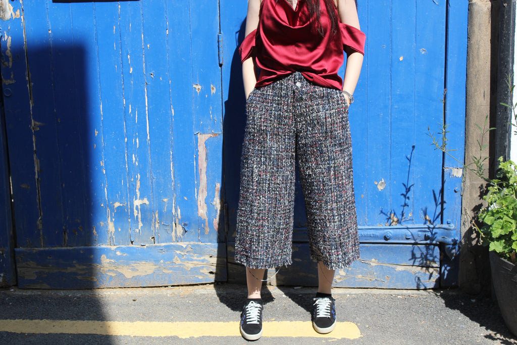 Person wearing a red top and patterned pants standing in front of a blue wall. Cut out burgundy top — handmade burgundy designer top with cut-out detail from Maryallé Jakarta, fitted, limited edition