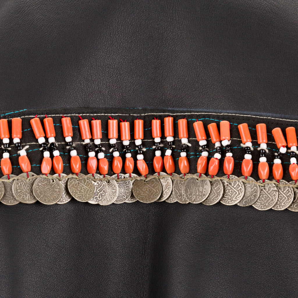 Close-up of a black fabric with orange beaded and coin-studded trim. Jewelled biker jacket — handmade designer biker jacket with jewel detailing from Hanout Boutique Marrakech, fitted, limited edition