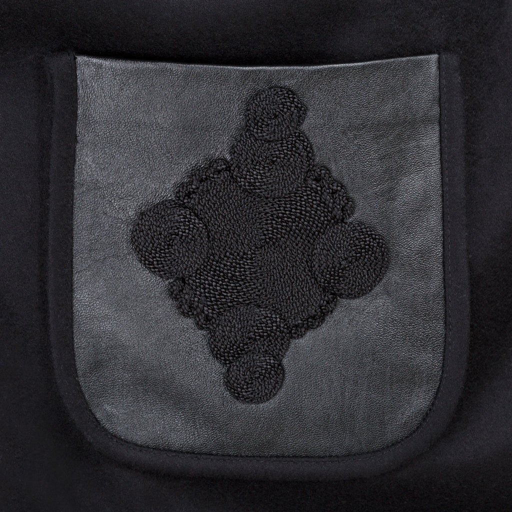 Black embroidered design on a gray pocket of a dark fabric garment. Wool embroidered coat — heavy wool designer coat with hand-embroidered detail from Hanout Boutique Marrakech, limited edition