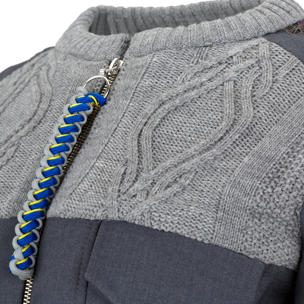 Close-up of a gray sweater with a blue and yellow braided zipper pull. Knitted bomber jacket — handmade designer knitted bomber from Patrick Owen Jakarta, relaxed fit, limited edition winter piece