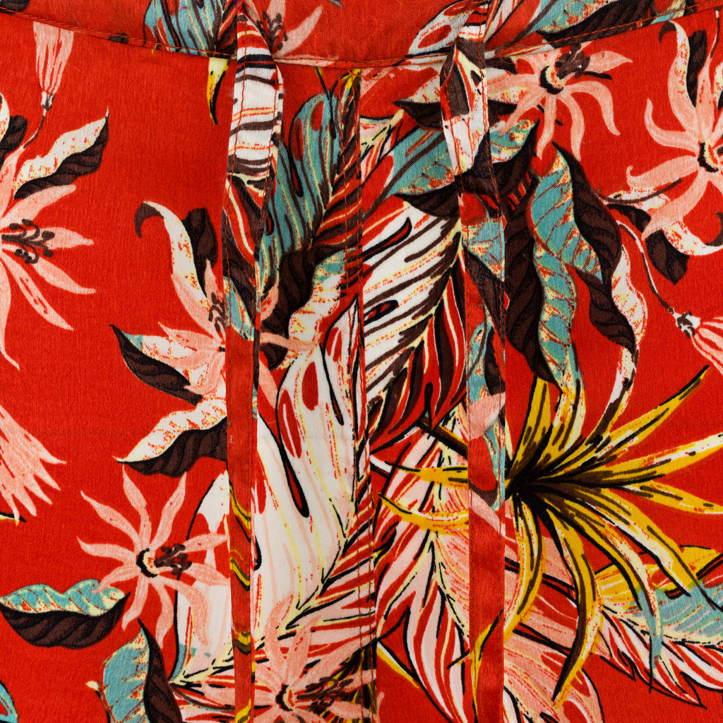 Close-up of a vibrant floral fabric pattern on a red background. Orange patterned silk pants — handmade orange silk designer pants with vibrant print from Hanout Boutique Marrakech, relaxed fit
