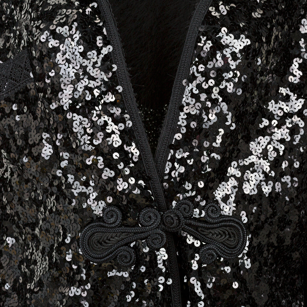 Close-up of black sequin fabric with decorative bow. Black sequins embroidered coat — black designer coat with hand-stitched sequin embroidery from Laure Welfling Marrakech, limited edition