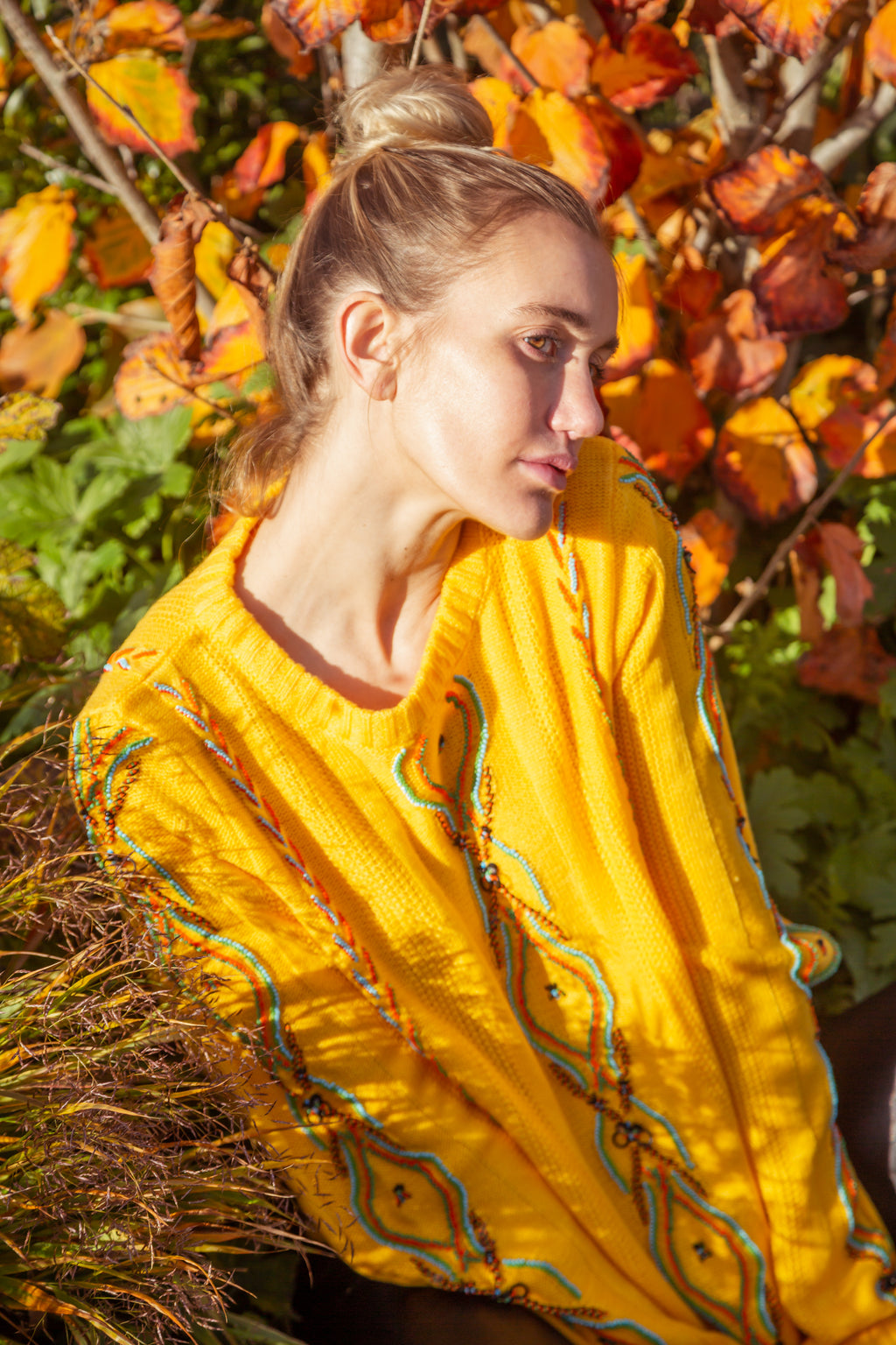 Woman in a yellow dress sitting among autumn leaves. Yellow bug wool jumper — handmade yellow wool designer jumper with bug print from Patrick Owen Jakarta, relaxed fit, limited edition