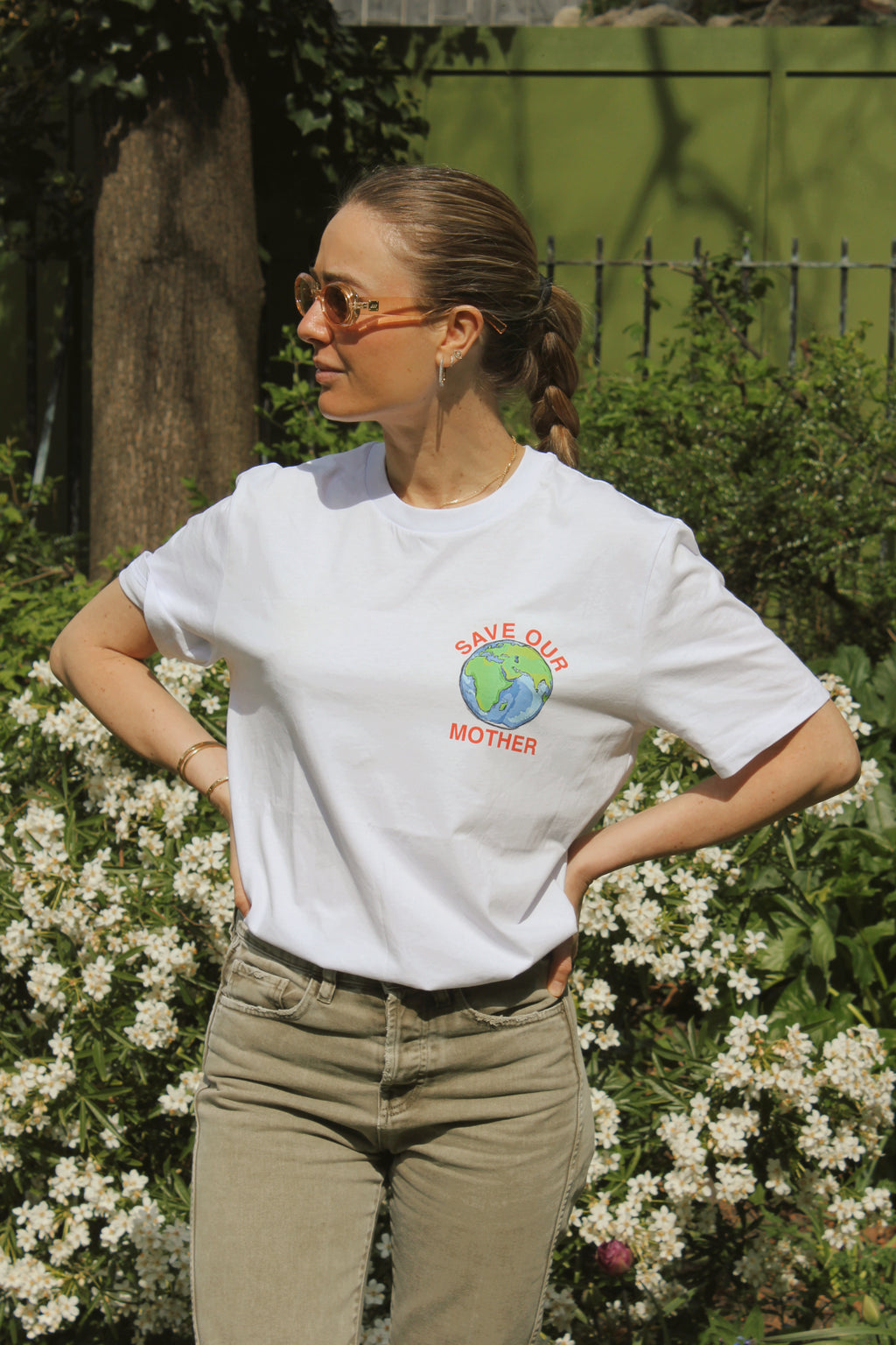 Save Our Mother climate tee — white organic cotton t-shirt with hand-illustrated earth print, unisex fit, climate charity tee. Girl in the city crossing the street with bottega bag