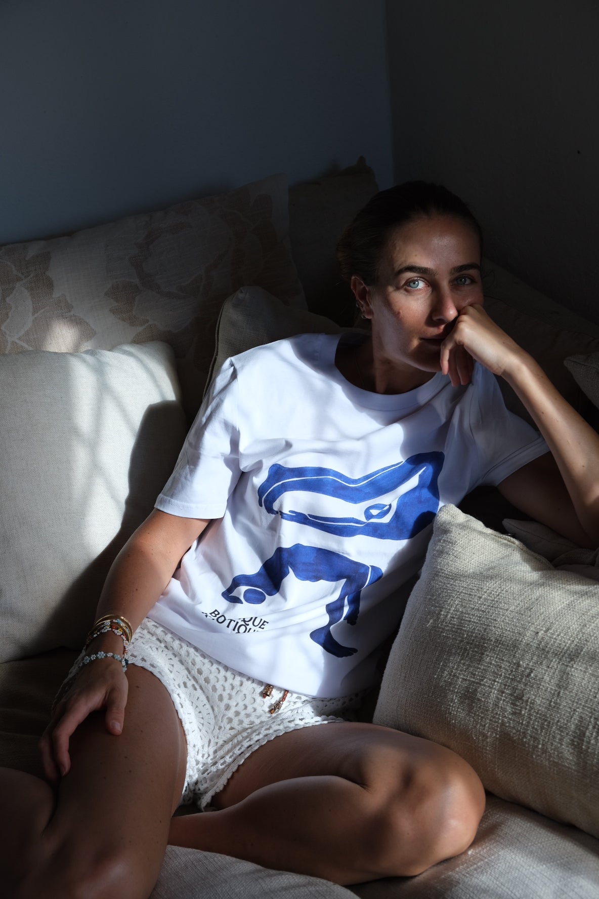 Person wearing a white t-shirt with blue graphics, sitting on a couch.