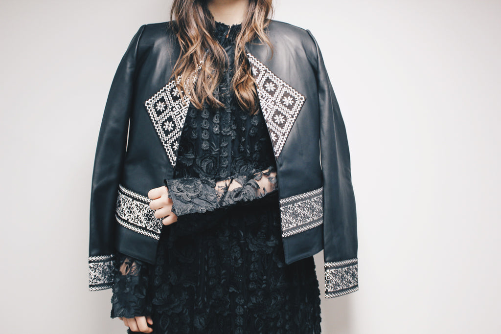 Person wearing a black leather jacket with white embroidery on a plain background. Black lace dress — handmade black lace designer dress from Hanout Boutique Marrakech, fitted, limited edition occasion piece