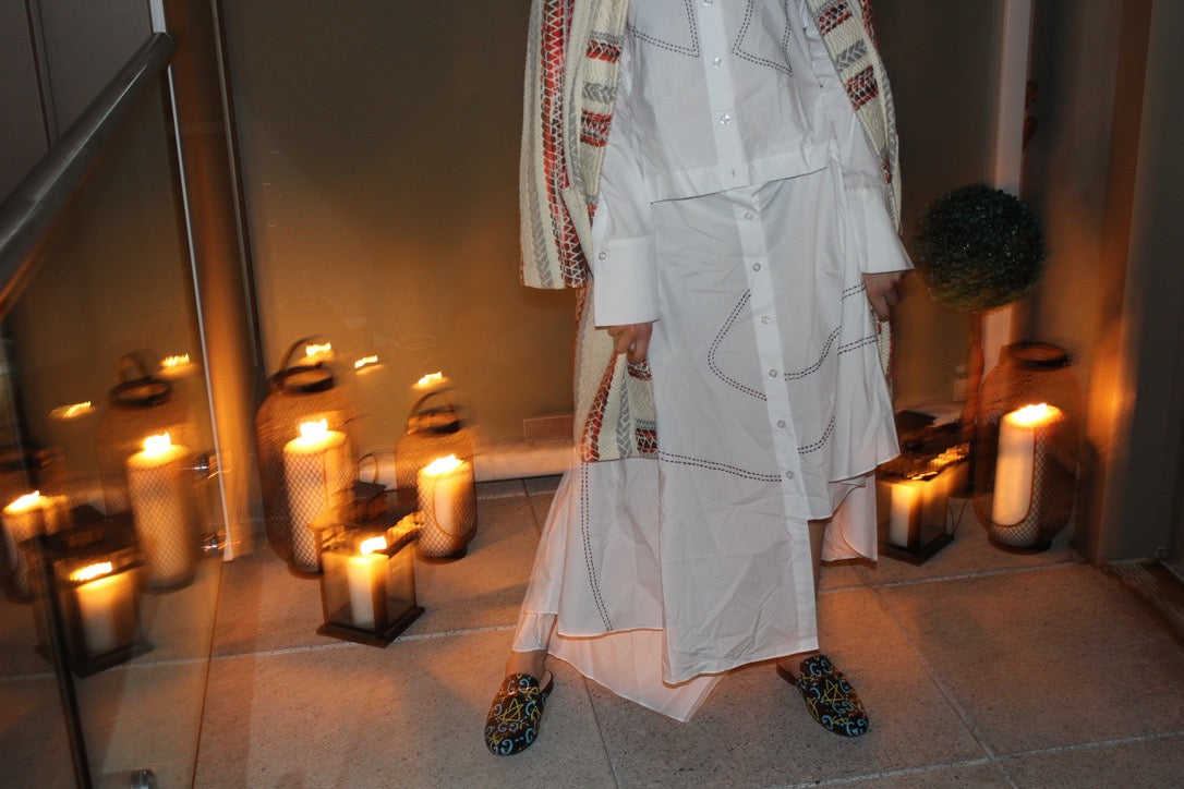 Person wearing a white outfit with geometric patterns in a room with candles and a mirror. Indonesian asymmetrical dress — handmade asymmetric designer dress from Major Minor Jakarta, relaxed fit, limited edition