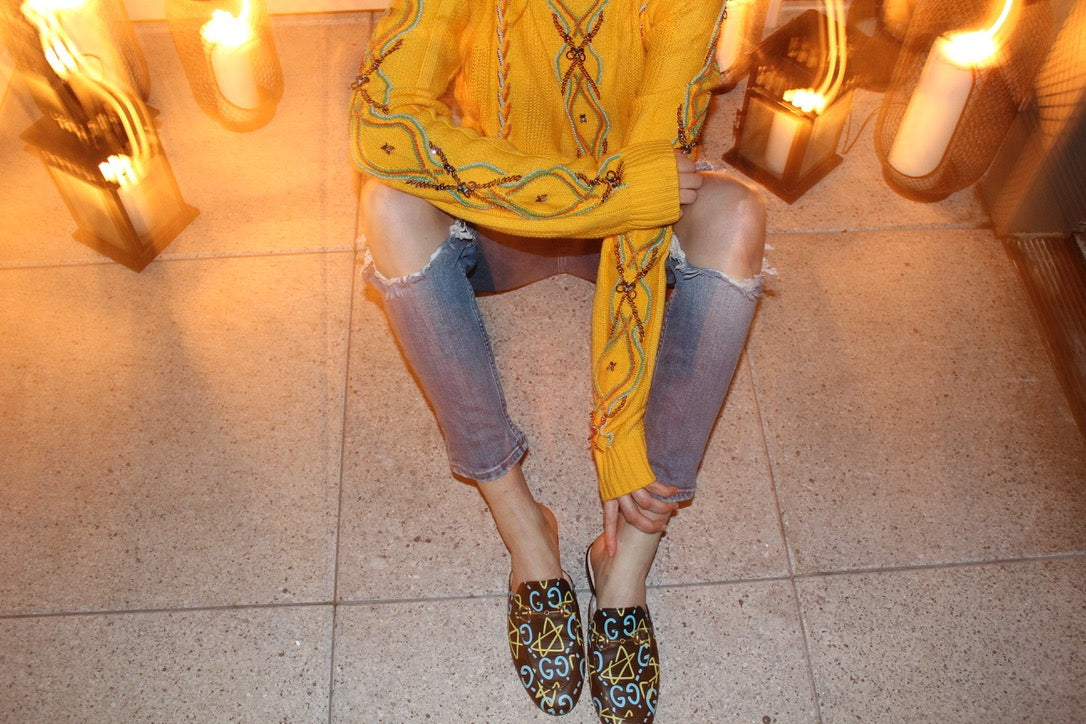 Person wearing a yellow embroidered top and ripped jeans with patterned shoes on a tiled floor. Yellow bug wool jumper — handmade yellow wool designer jumper with bug print from Patrick Owen Jakarta, relaxed fit, limited edition