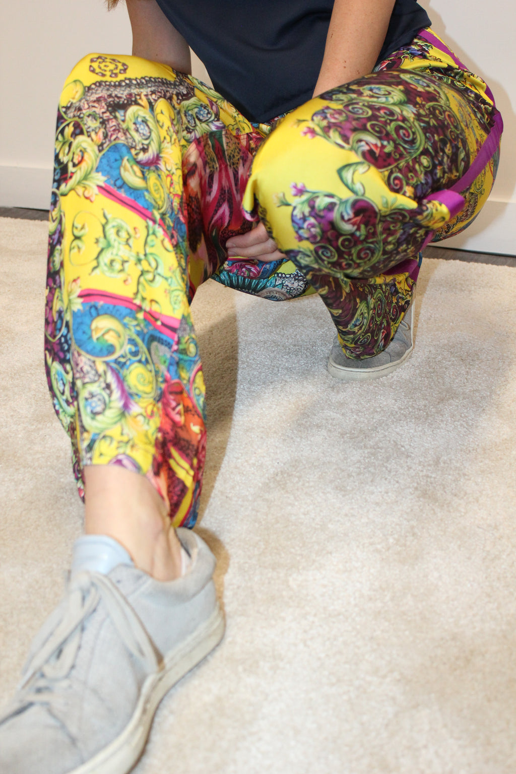 Person wearing colorful patterned pants sitting on a white couch. Yellow patterned silk pants — handmade yellow silk designer pants with groovy print from Hanout Boutique Marrakech, relaxed fit