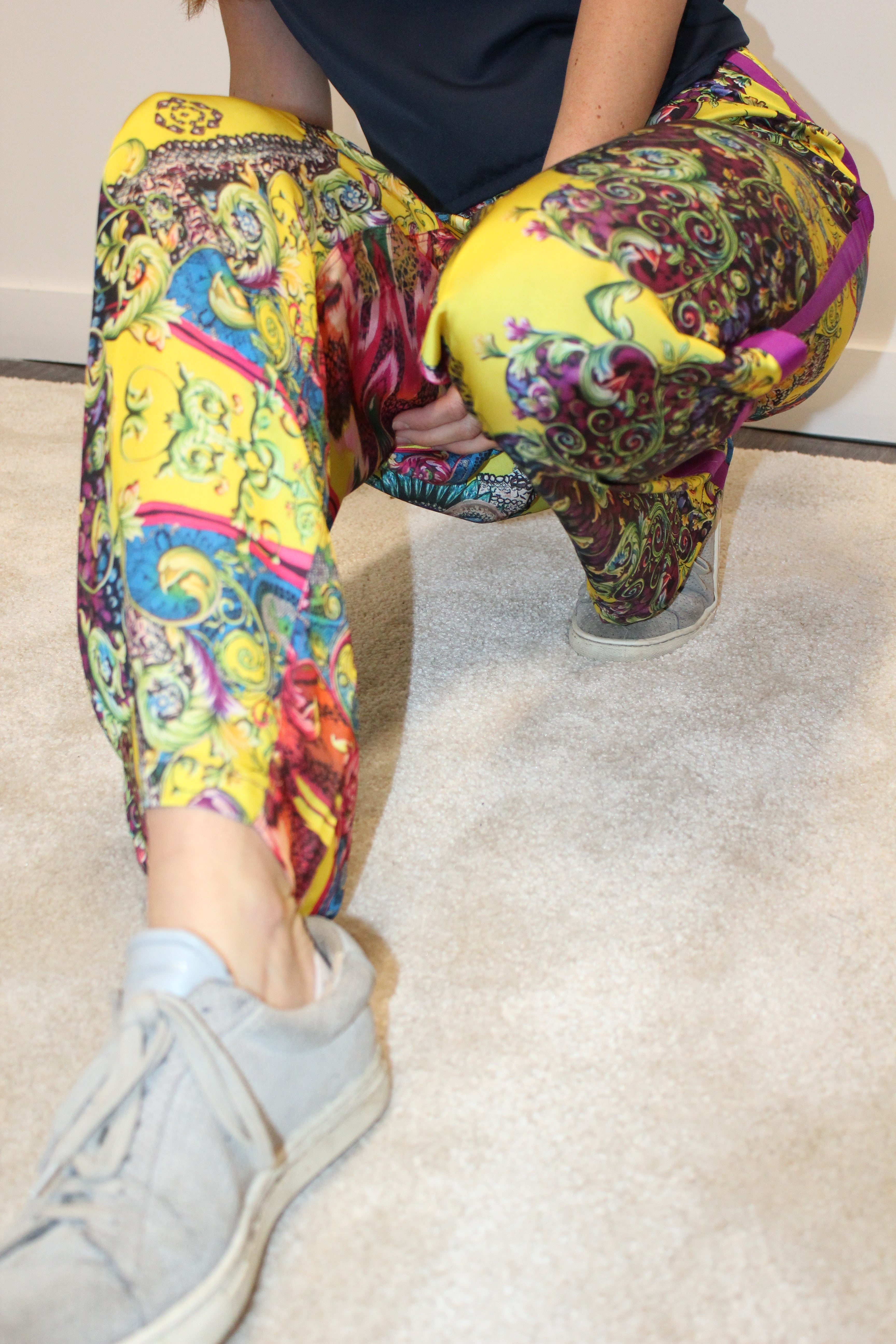 Person wearing colorful patterned pants sitting on a white couch. Yellow patterned silk pants — handmade yellow silk designer pants with groovy print from Hanout Boutique Marrakech, relaxed fit