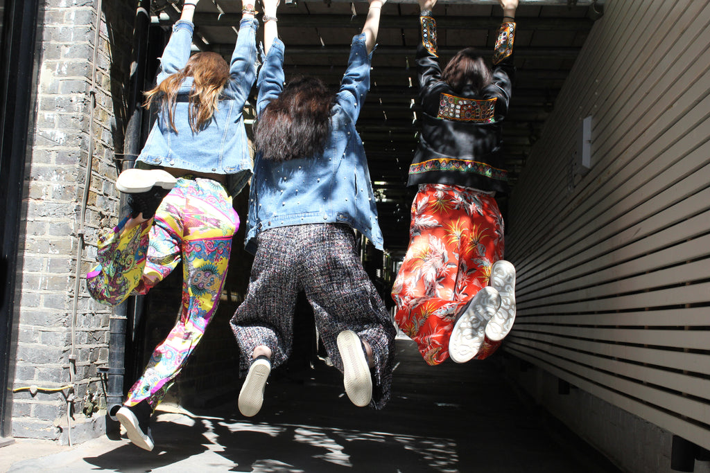 Three people hanging from a handrail on a sunny day. Yellow patterned silk pants — handmade yellow silk designer pants with groovy print from Hanout Boutique Marrakech, relaxed fit