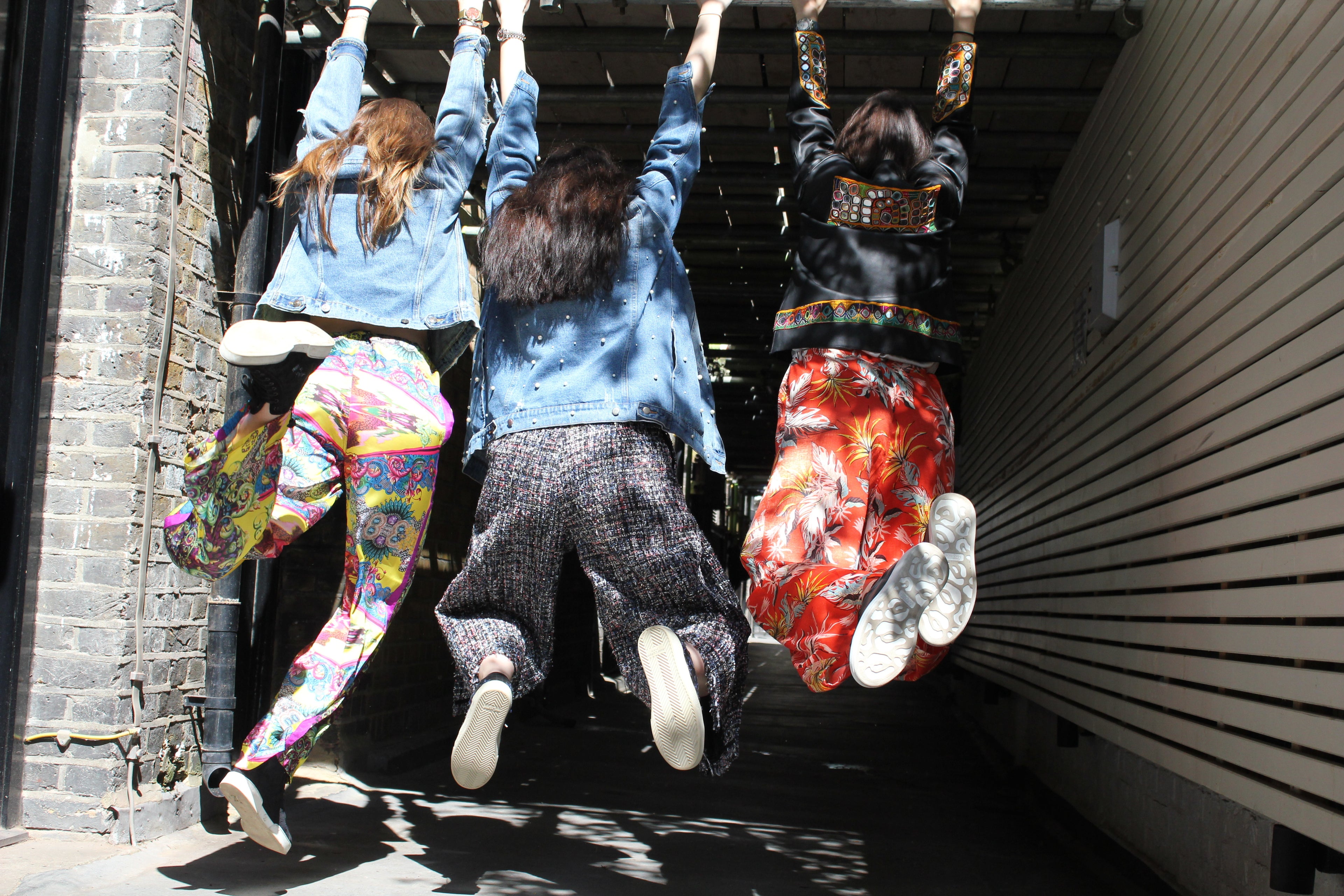 Three people hanging from a handrail on a sunny day. Yellow patterned silk pants — handmade yellow silk designer pants with groovy print from Hanout Boutique Marrakech, relaxed fit