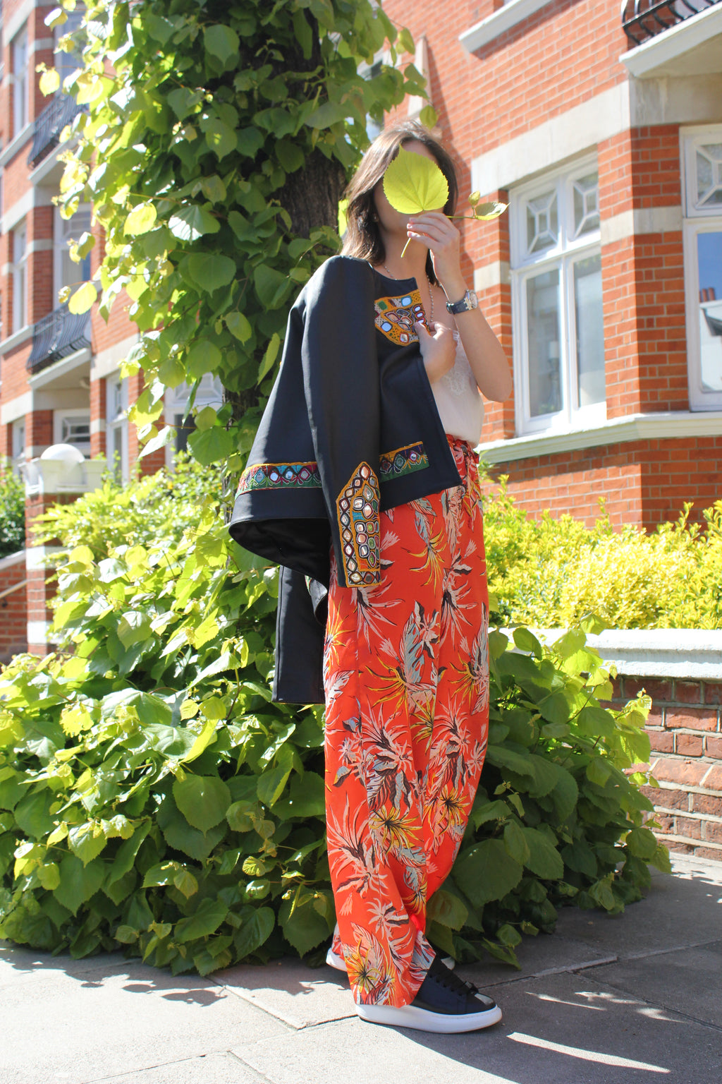 Person with colorful trousers in front of greenery and buildings. Orange patterned silk pants — handmade orange silk designer pants with vibrant print from Hanout Boutique Marrakech, relaxed fit