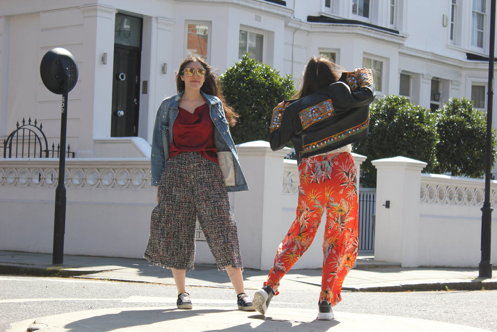Two women walking on a street with a white building in the background. Orange patterned silk pants — handmade orange silk designer pants with vibrant print from Hanout Boutique Marrakech, relaxed fit