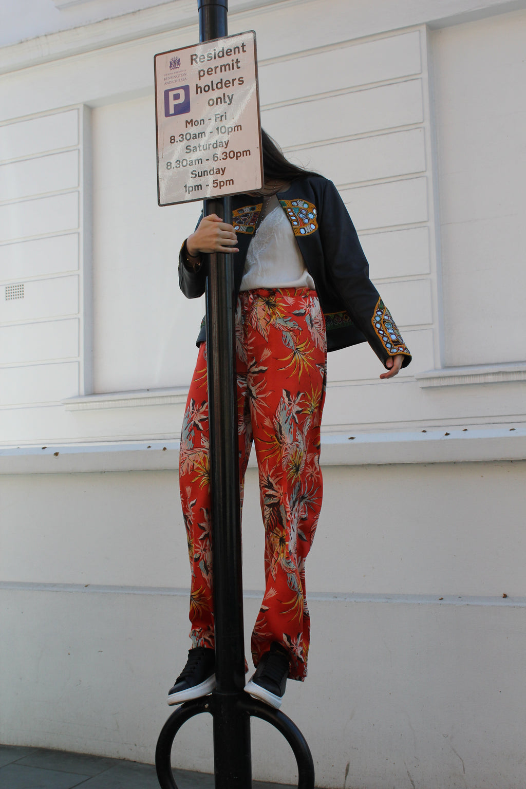 Person wearing a colorful floral dress holding a parking sign in front of a white door. Orange patterned silk pants — handmade orange silk designer pants with vibrant print from Hanout Boutique Marrakech, relaxed fit