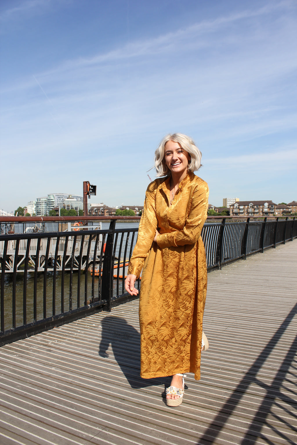 Person wearing a gold dress standing on a rooftop with a cityscape in the background. Golden Hour dress — handmade yellow gold designer dress from Hanout Boutique Marrakech, fitted, limited edition occasion piece