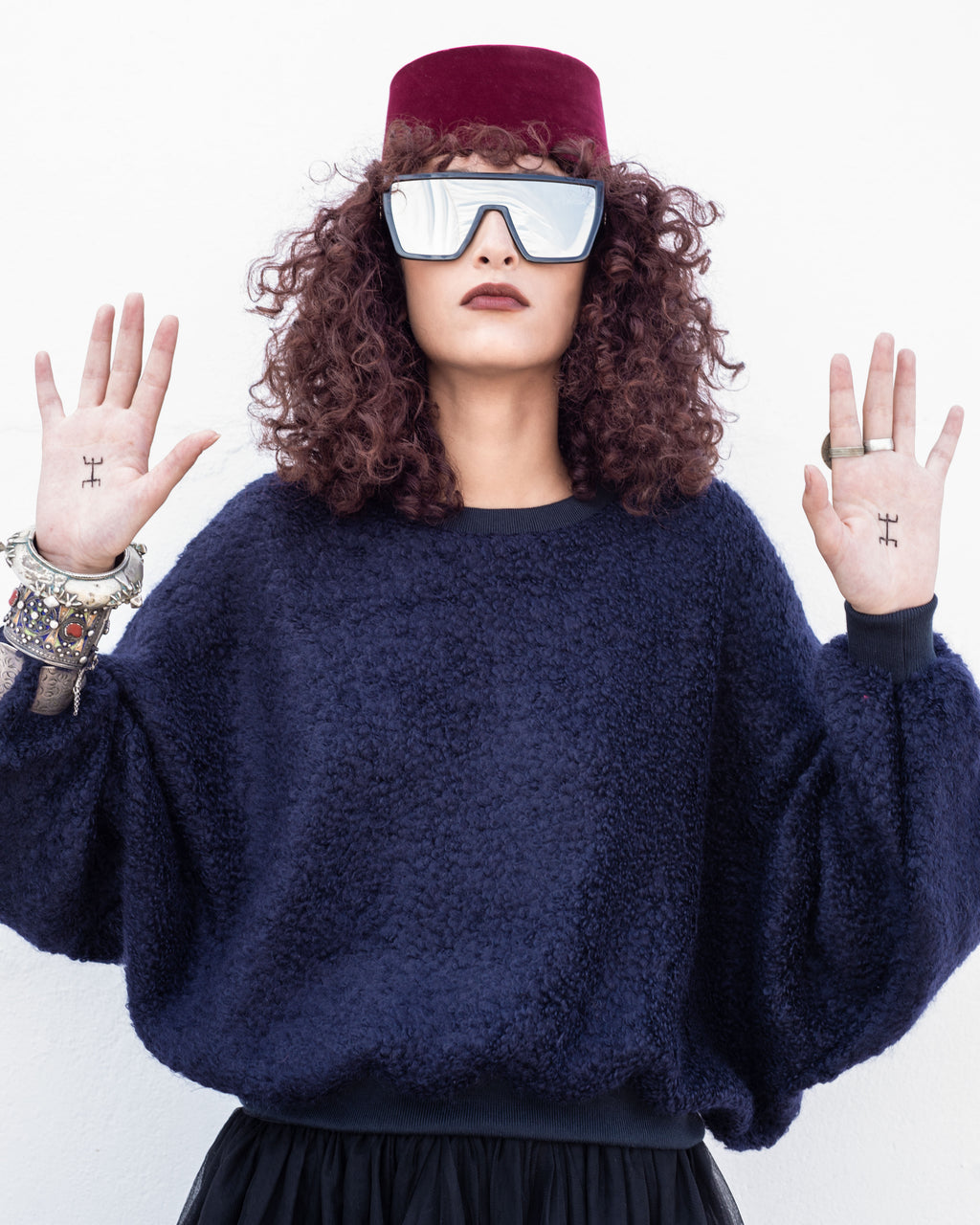 Person wearing a dark blue sweater and a maroon hat with reflective sunglasses, on a white background. Navy wool cashmere jumper — handmade navy wool blend designer jumper from Hanout Boutique Marrakech, relaxed fit, limited edition