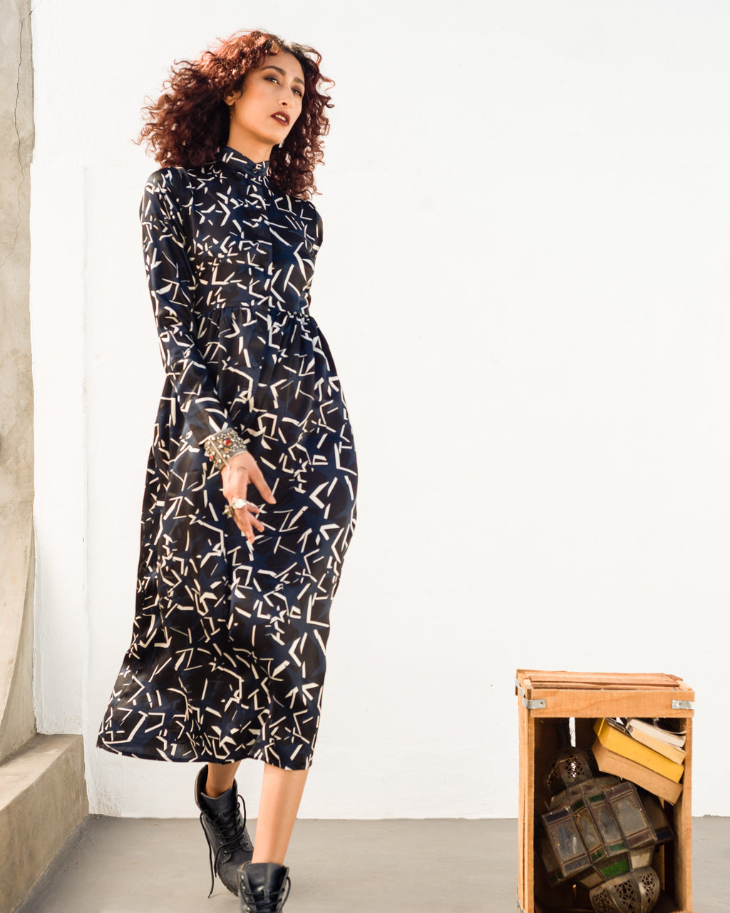 Woman wearing a black patterned dress standing next to a wooden suitcase. Starry Night dress — handmade designer dress with starry print from Hanout Boutique Marrakech, fitted, limited edition occasion piece