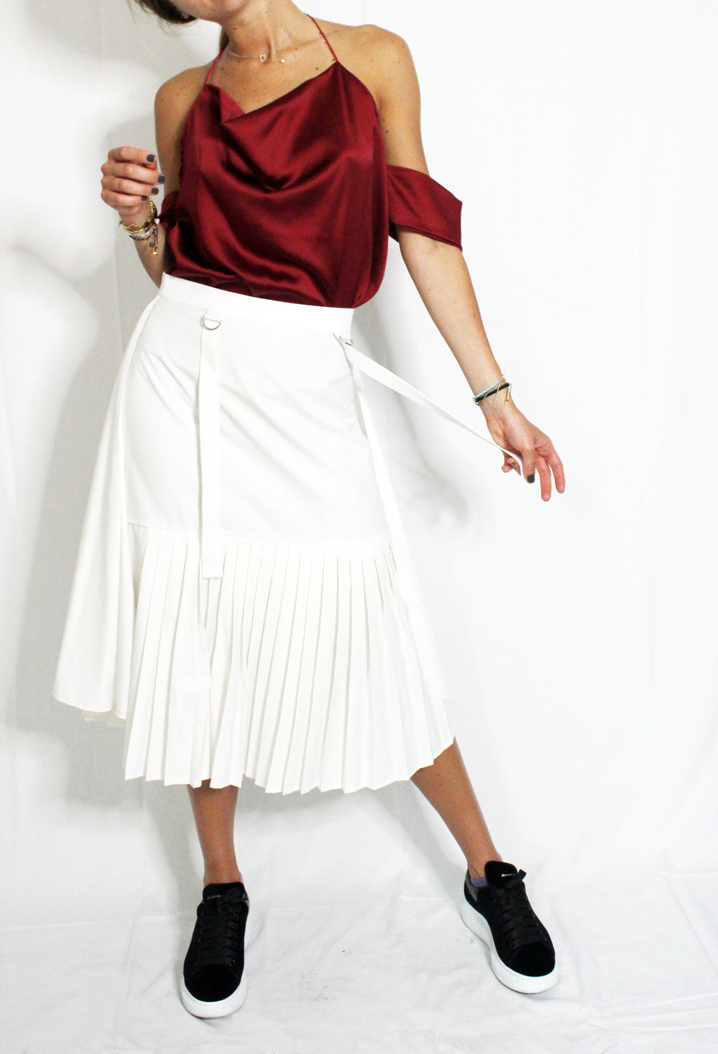 Person wearing a red off-shoulder top and white pleated skirt on a plain background. Indonesian asymmetrical skirt — handmade asymmetric designer skirt from Major Minor Jakarta, relaxed fit, limited edition