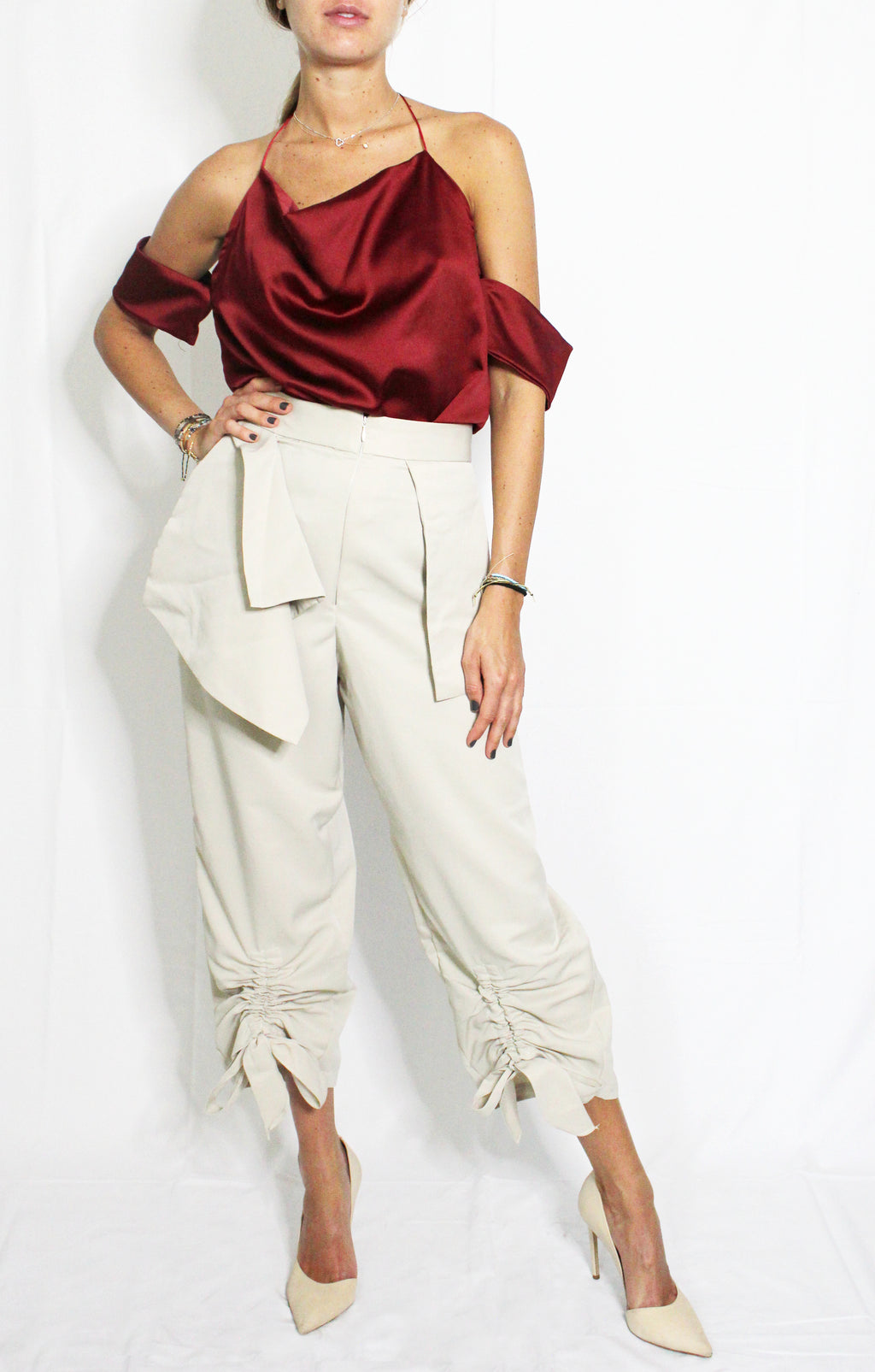 Person wearing a burgundy satin top and beige pants on a white background. Cut out burgundy top — handmade burgundy designer top with cut-out detail from Maryallé Jakarta, fitted, limited edition