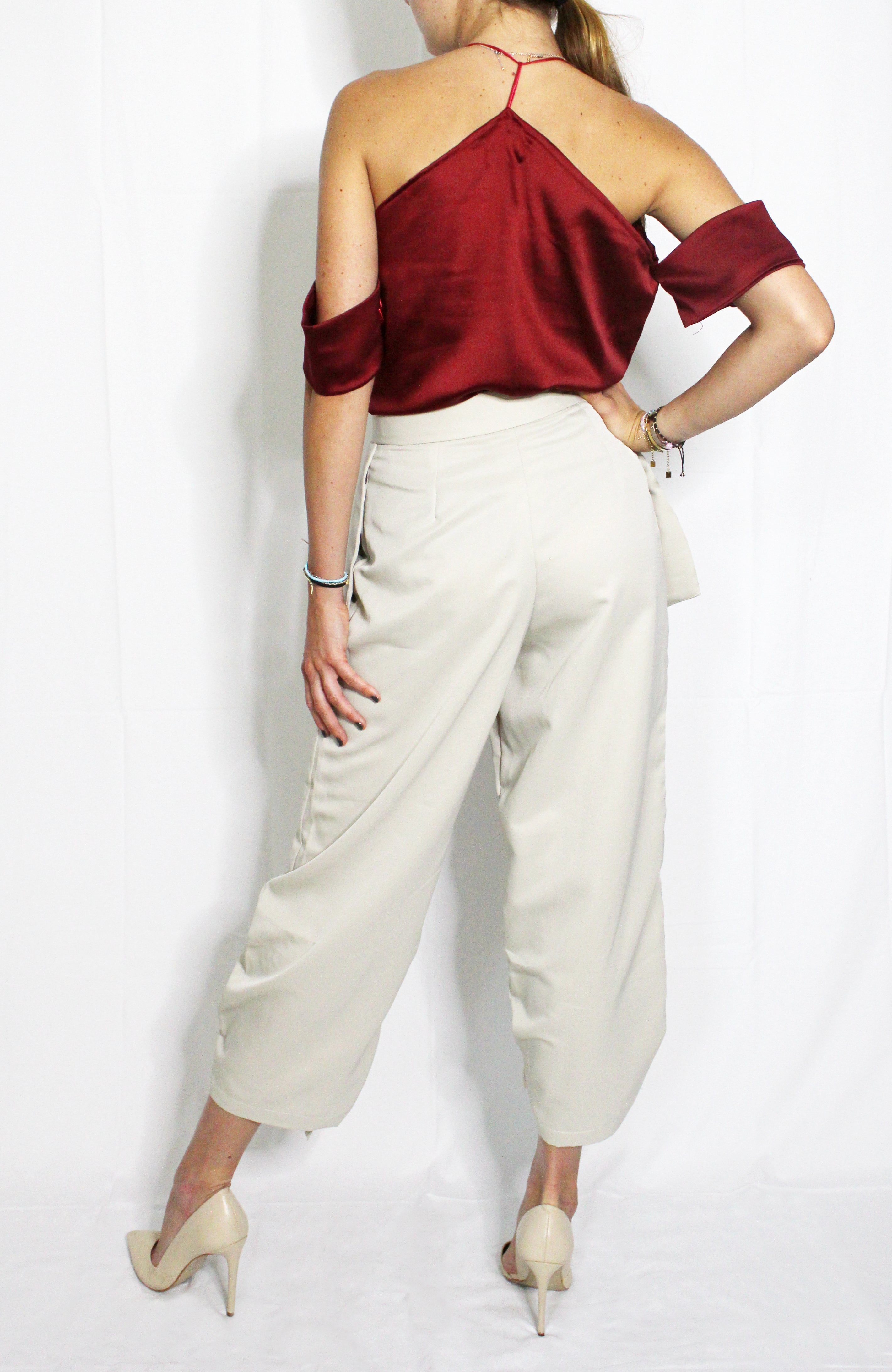 Person wearing a burgundy off-shoulder top and white wide-leg pants on a light background. Cut out burgundy top — handmade burgundy designer top with cut-out detail from Maryallé Jakarta, fitted, limited edition