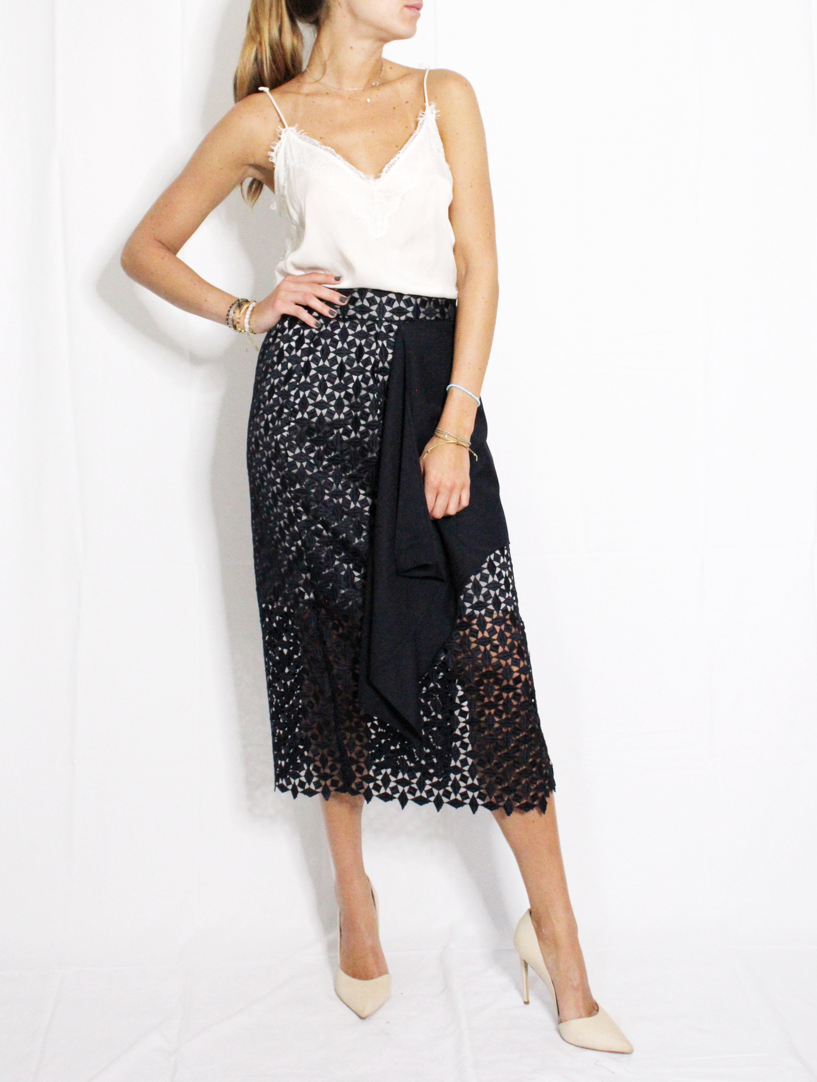 Woman wearing a white top and black patterned skirt on a white background. Indonesian-inspired lace skirt — handmade lace designer skirt from Maryallé Jakarta, fitted, limited edition occasion piece