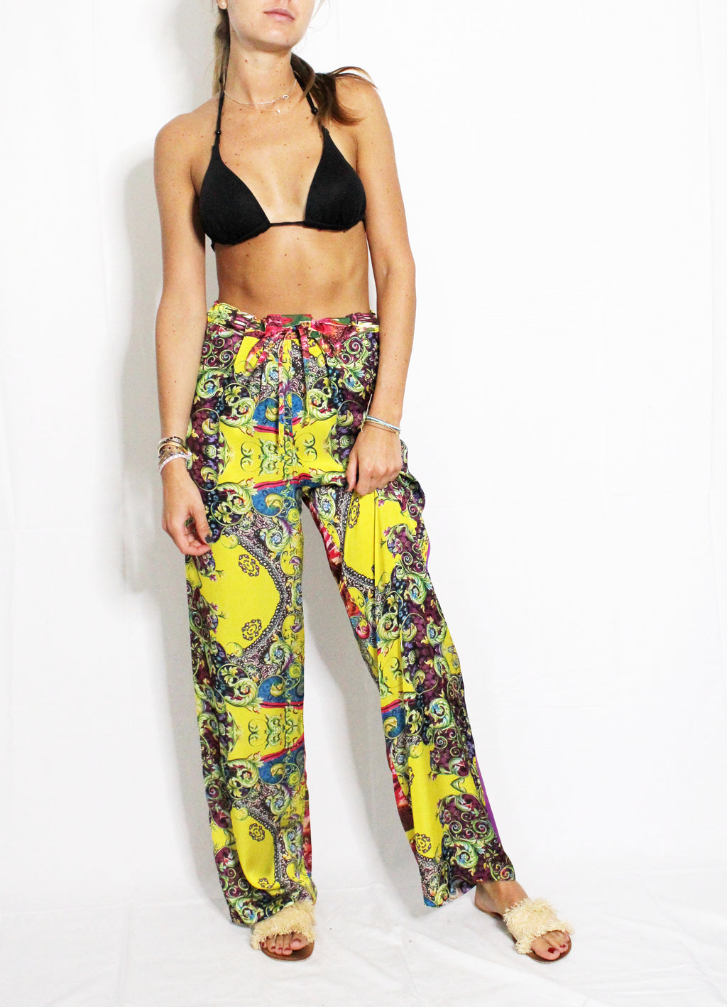 Woman wearing a black bikini top and colorful patterned pants on a white background. Yellow patterned silk pants — handmade yellow silk designer pants with groovy print from Hanout Boutique Marrakech, relaxed fit