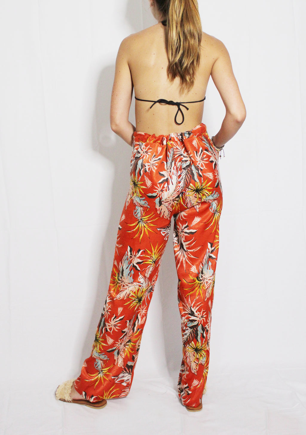 Person wearing a strapless top and red floral pants on a white background. Orange patterned silk pants — handmade orange silk designer pants with vibrant print from Hanout Boutique Marrakech, relaxed fit