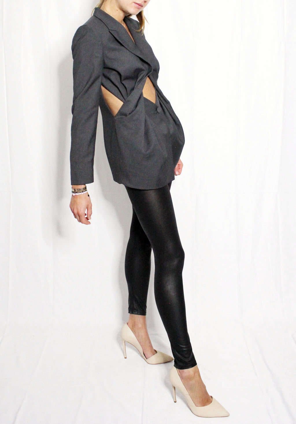Person wearing a gray blazer with cut-out design and black leather leggings on a white background. Unique ultra feminine cut blazer — handmade designer blazer from Patrick Owen Jakarta, fitted, limited edition occasion piece