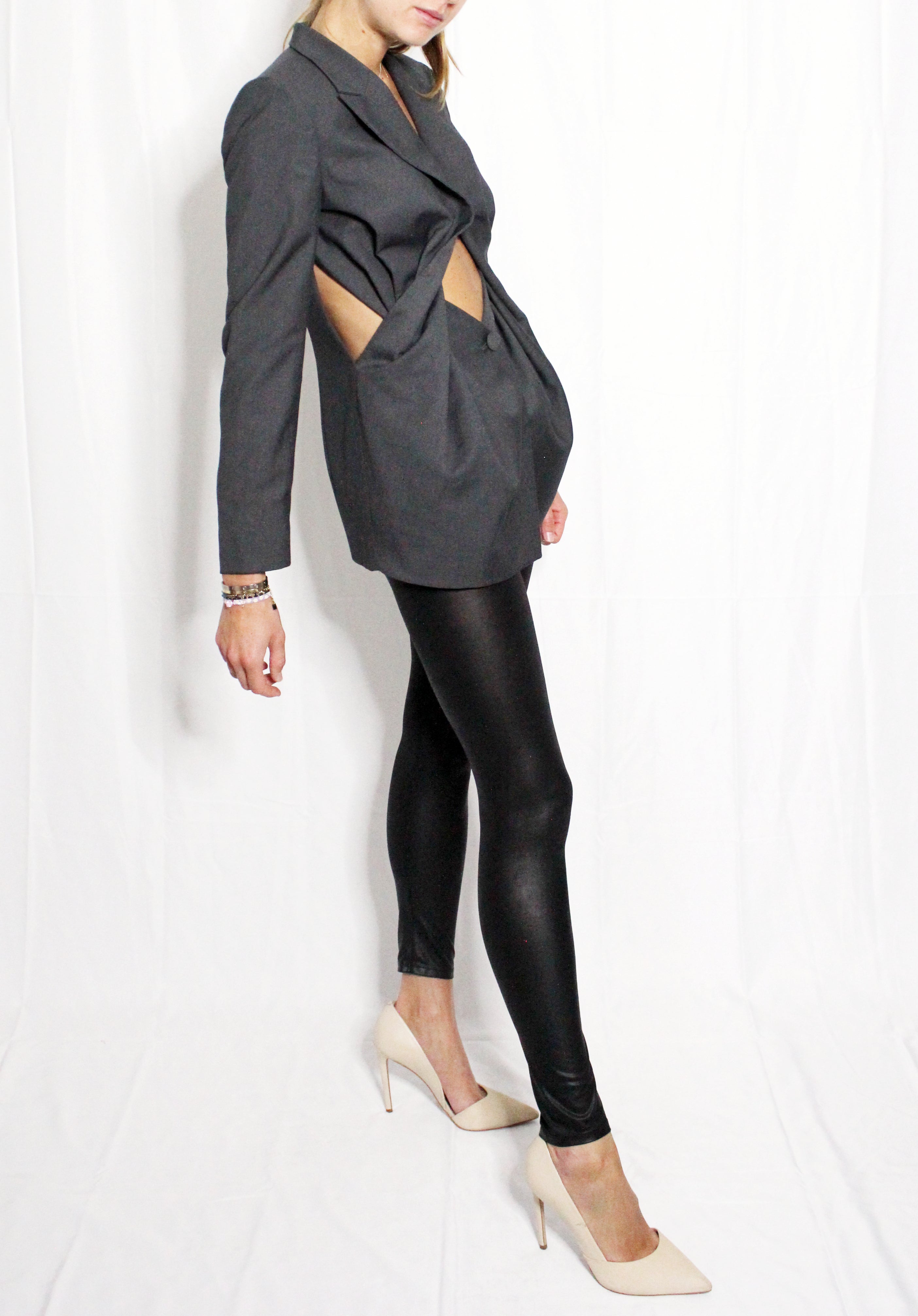 Person wearing a gray blazer with cut-out design and black leather leggings on a white background. Unique ultra feminine cut blazer — handmade designer blazer from Patrick Owen Jakarta, fitted, limited edition occasion piece