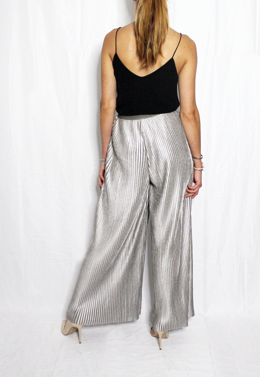Woman wearing a black top and silver pleated pants on a white background. Silver velvet trousers — handmade silver velvet designer trousers from Patrick Owen Jakarta, tailored fit, limited edition
