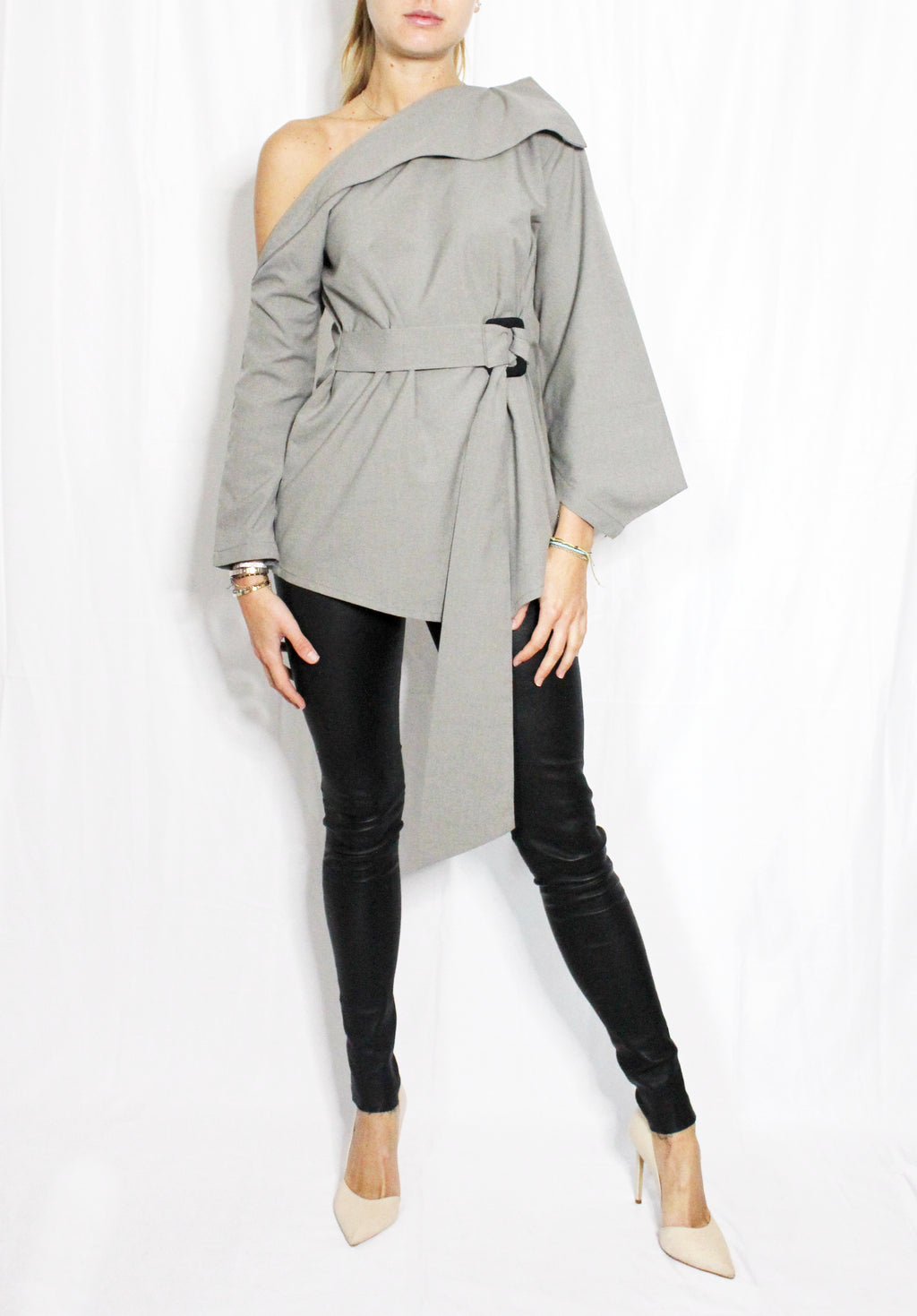 Woman wearing a gray one-shoulder top and black pants on a white background. Indonesian asymmetrical blouse — handmade asymmetric designer blouse from Maryallé Jakarta, fitted, limited edition piece