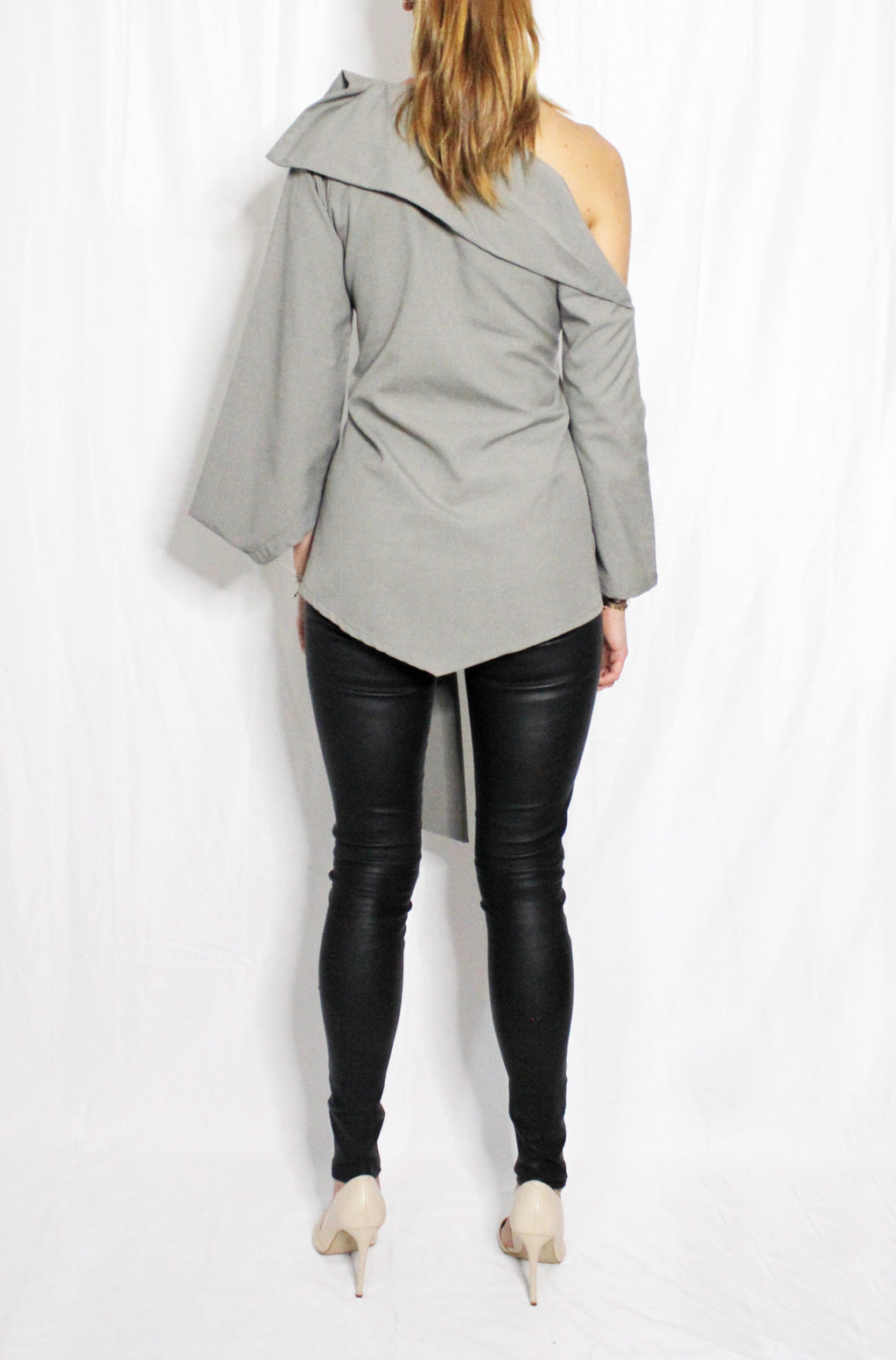 Person wearing a gray off-shoulder top and black leather pants on a white background. Indonesian asymmetrical blouse — handmade asymmetric designer blouse from Maryallé Jakarta, fitted, limited edition piece