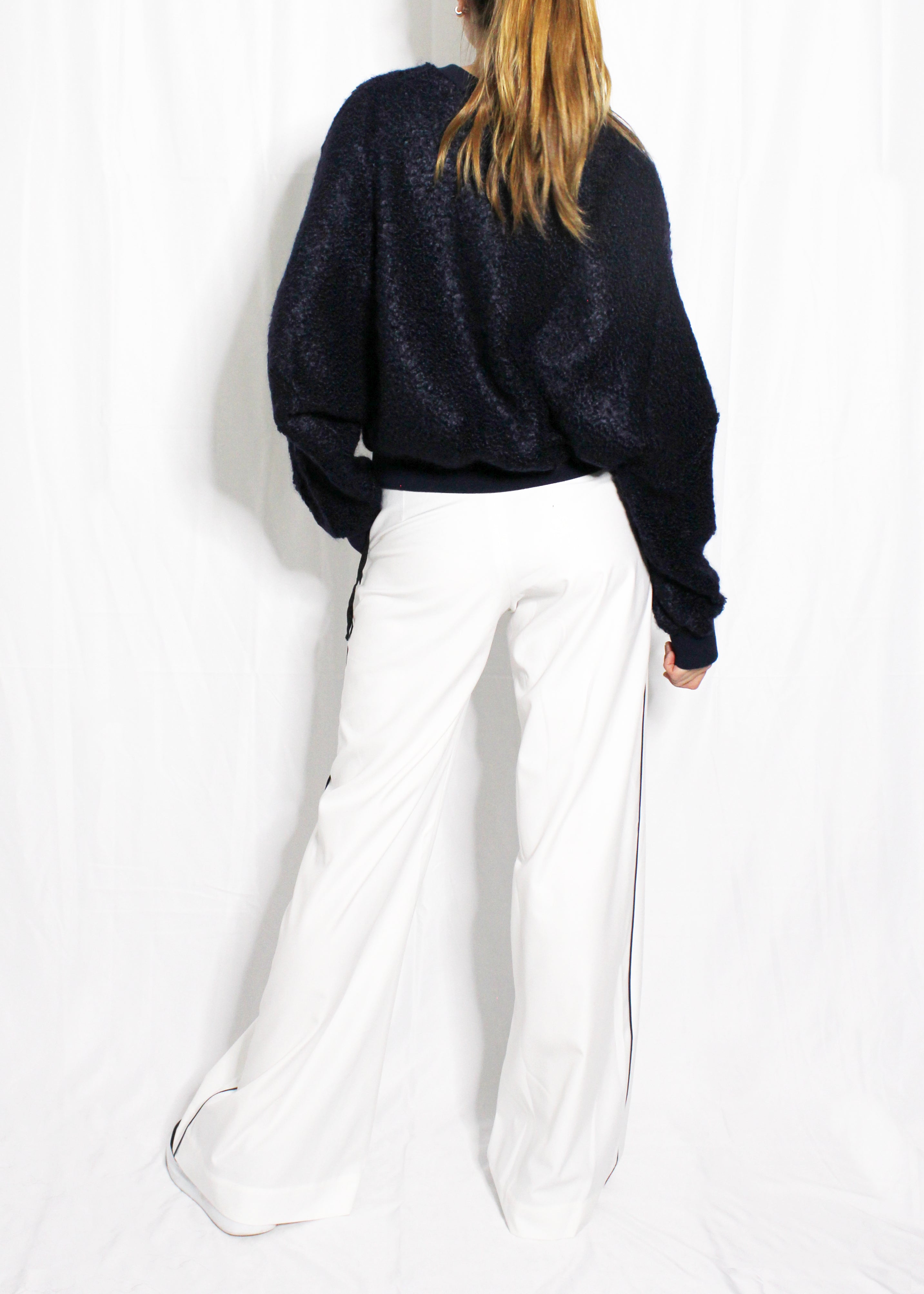 Person wearing a navy sweater and white pants against a white background. Extra loose trousers — handmade designer relaxed trousers from Major Minor Jakarta, oversized fit, limited edition summer