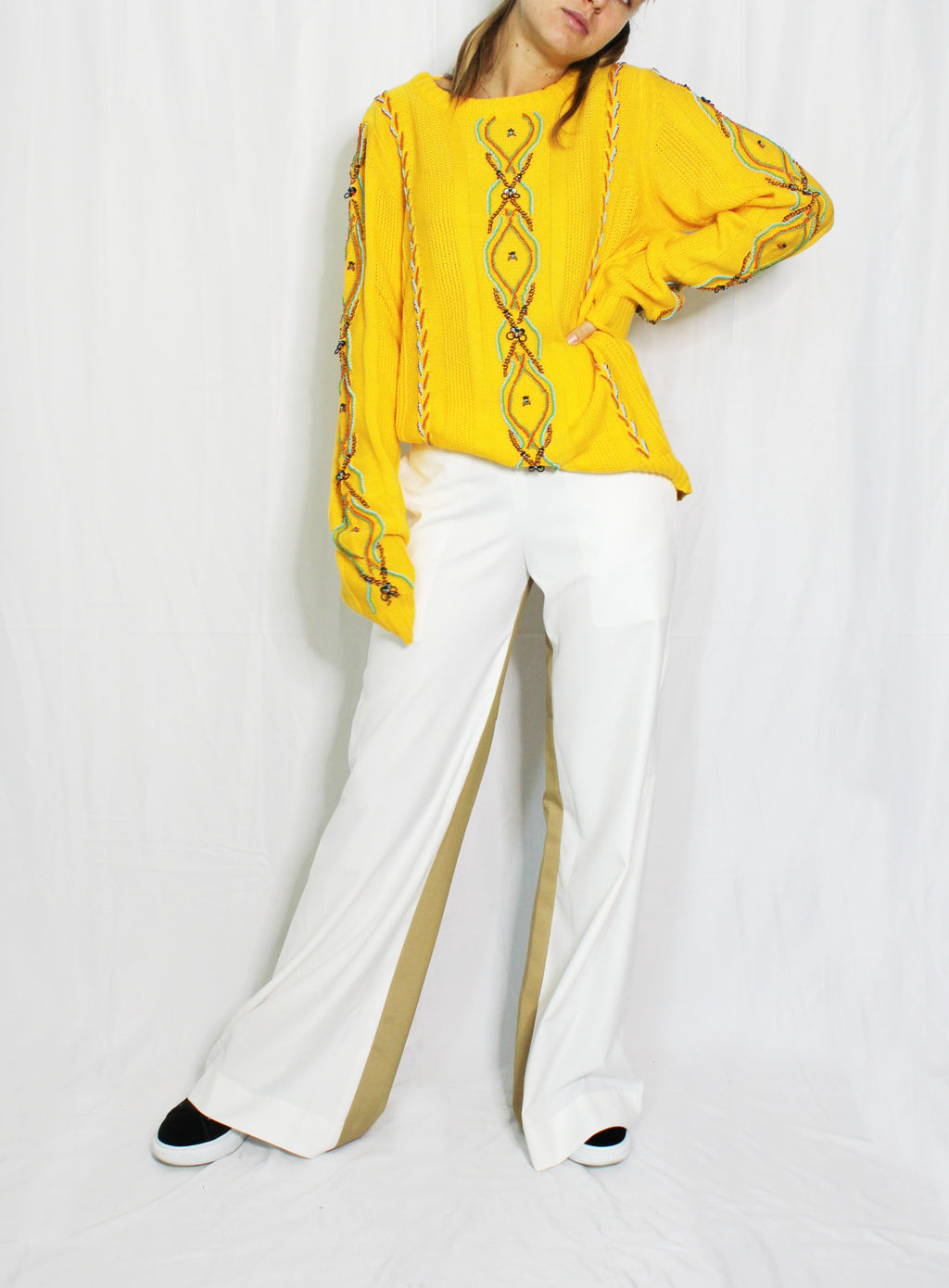 Person wearing a yellow embroidered blouse and white pants on a white background. Yellow bug wool jumper — handmade yellow wool designer jumper with bug print from Patrick Owen Jakarta, relaxed fit, limited edition. Double coloured trousers — handmade designer two-tone trousers from Major Minor Jakarta, relaxed fit, limited edition piece