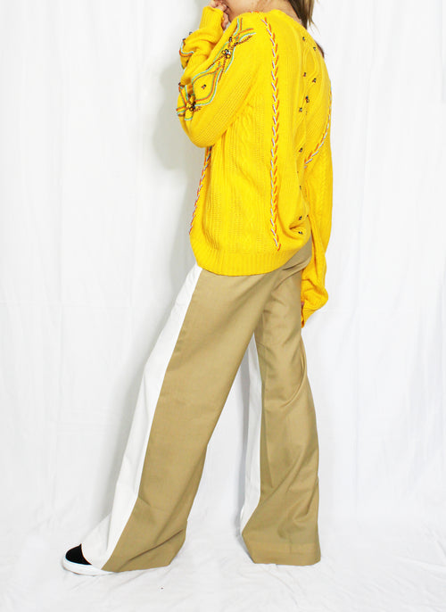Person wearing a bright yellow jacket and beige pants on a white background. Yellow bug wool jumper — handmade yellow wool designer jumper with bug print from Patrick Owen Jakarta, relaxed fit, limited edition. Double coloured trousers — handmade designer two-tone trousers from Major Minor Jakarta, relaxed fit, limited edition piece