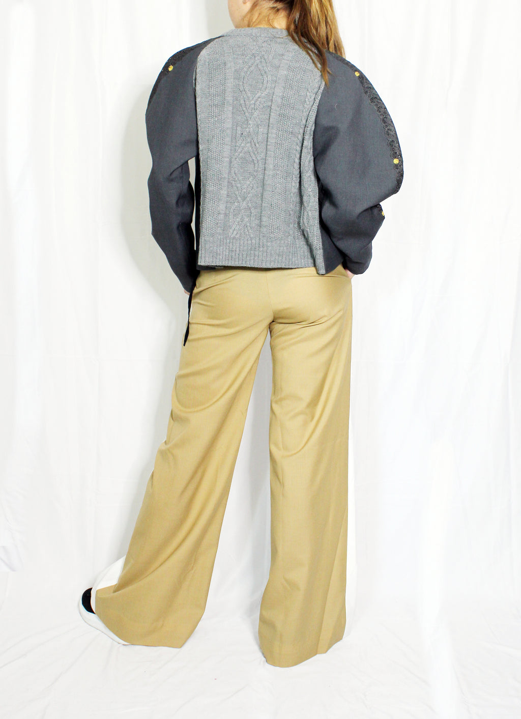 Person wearing a gray sweater with black sleeves and beige pants on a white background. Knitted bomber jacket — handmade designer knitted bomber from Patrick Owen Jakarta, relaxed fit, limited edition winter piece. Double coloured trousers — handmade designer two-tone trousers from Major Minor Jakarta, relaxed fit, limited edition piece