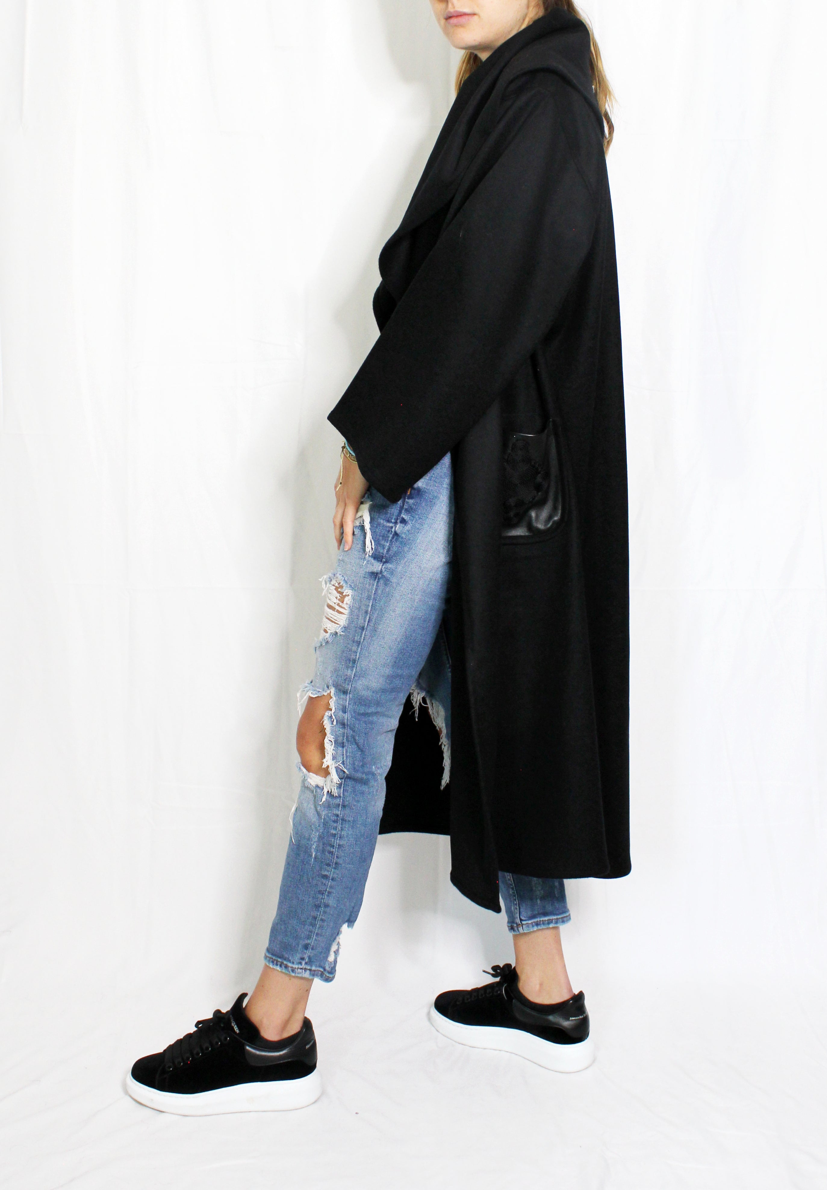 Person wearing a black coat, ripped jeans, and black shoes on a white background. Wool embroidered coat — heavy wool designer coat with hand-embroidered detail from Hanout Boutique Marrakech, limited edition