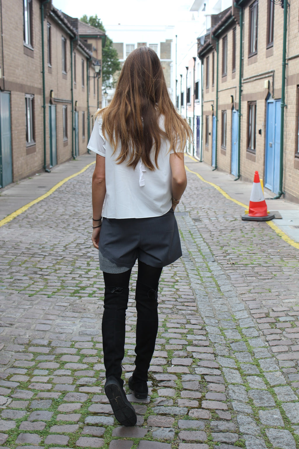 Person walking down a narrow street with buildings on either side. Wool blend shorts — handmade designer wool blend shorts from Patrick Owen Jakarta, tailored fit, limited edition piece