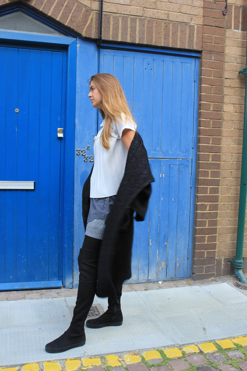 Woman standing in front of blue doors on a brick building. Wool blend shorts — handmade designer wool blend shorts from Patrick Owen Jakarta, tailored fit, limited edition piece