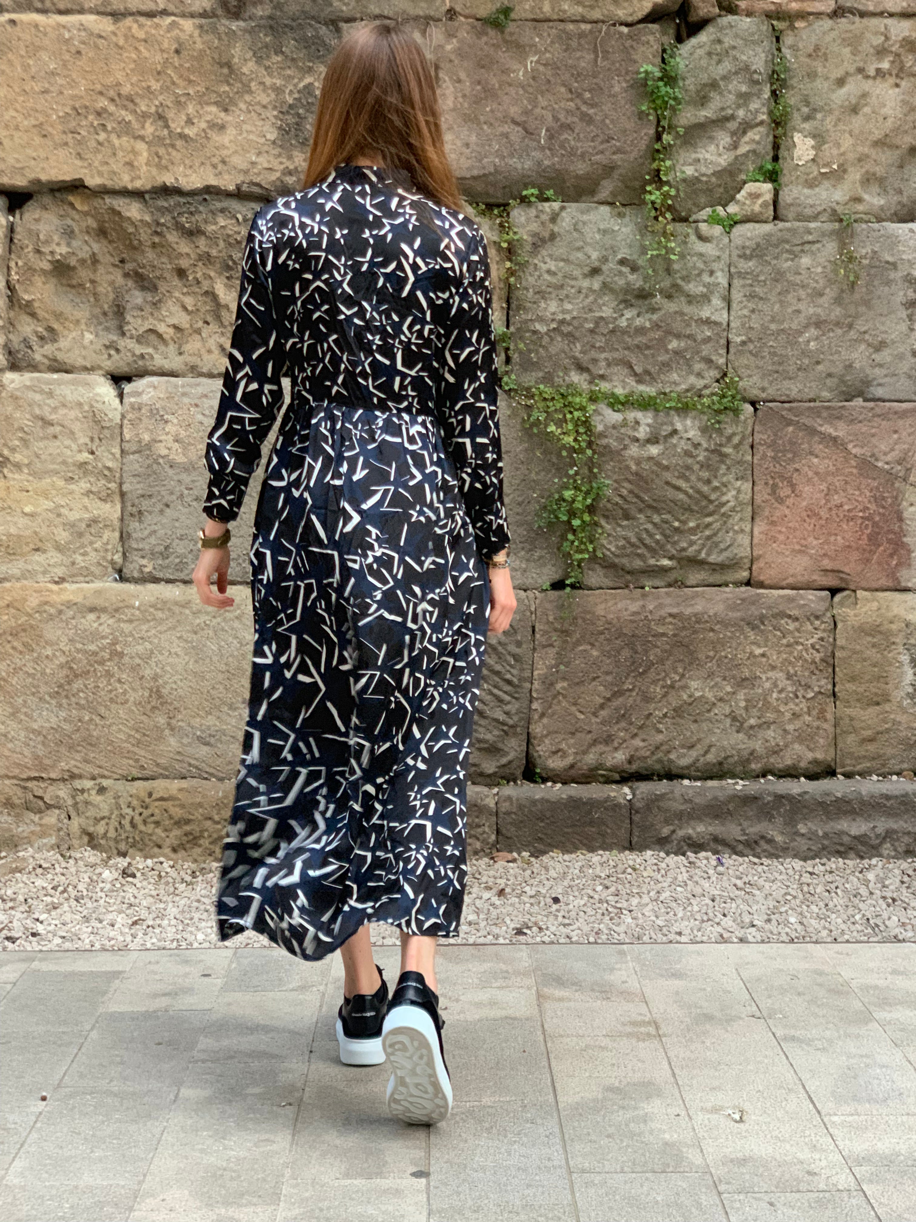 Person wearing a black and white patterned dress standing in front of a stone wall. Starry Night dress — handmade designer dress with starry print from Hanout Boutique Marrakech, fitted, limited edition occasion piece