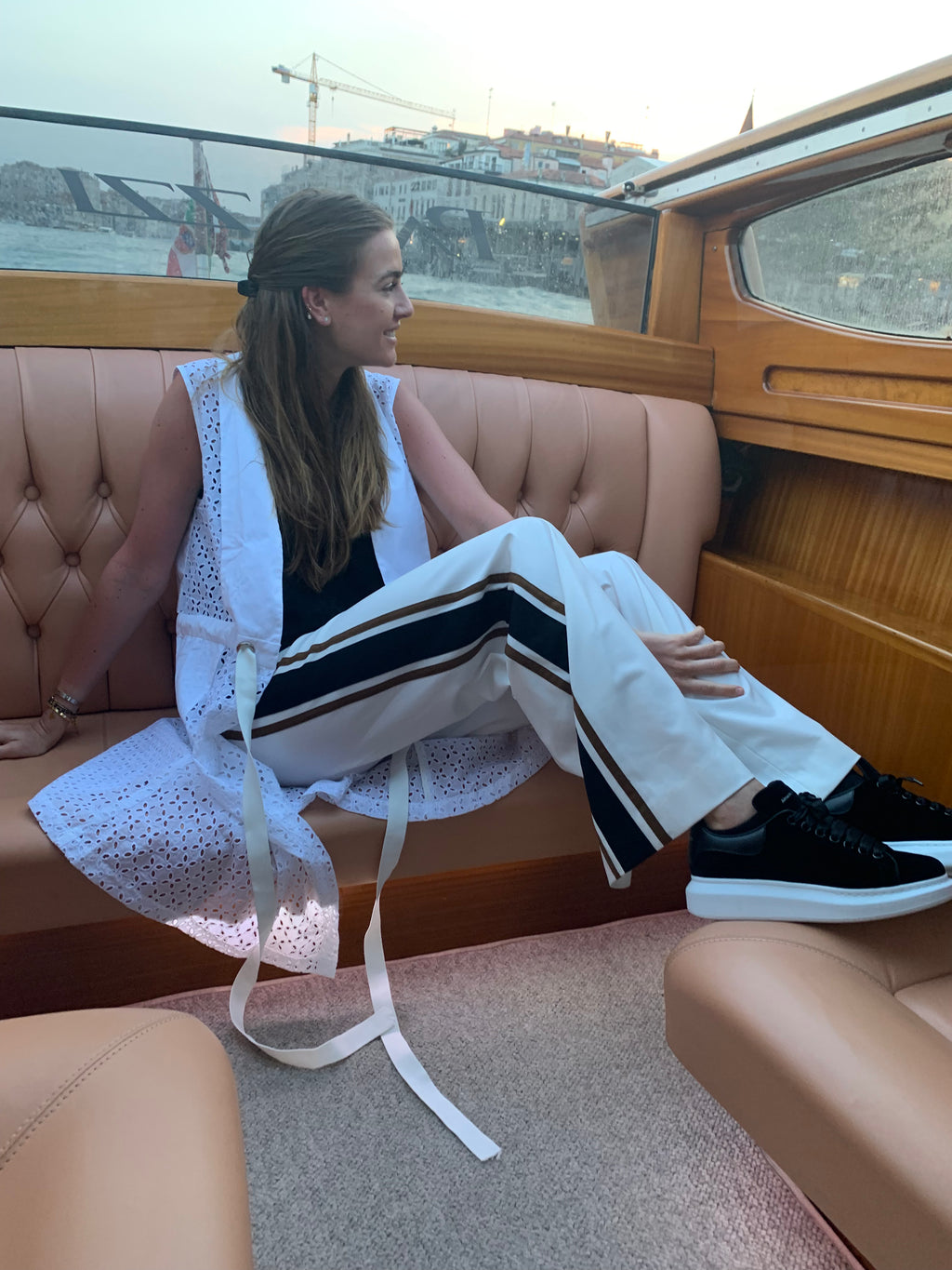 Woman sitting on a boat in Venice with a cityscape in the background. Striped trousers — handmade designer striped cotton trousers from Major Minor Jakarta, relaxed fit, limited edition summer. Indonesian cool summer vest — handmade designer cotton summer vest from Major Minor Jakarta, relaxed fit, limited edition