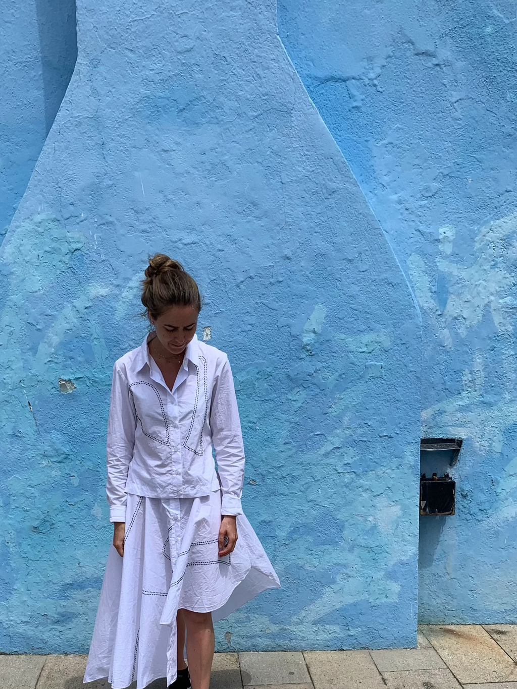 Person wearing a white outfit standing in front of a blue wall with a red object on the left. Indonesian asymmetrical dress — handmade asymmetric designer dress from Major Minor Jakarta, relaxed fit, limited edition