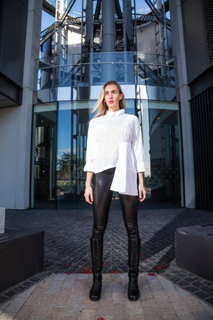 Woman in a white shirt and black leather pants standing in front of a modern building. White dotted blouse — handmade white designer blouse with delicate dot print from Major Minor Jakarta, relaxed fit, limited edition