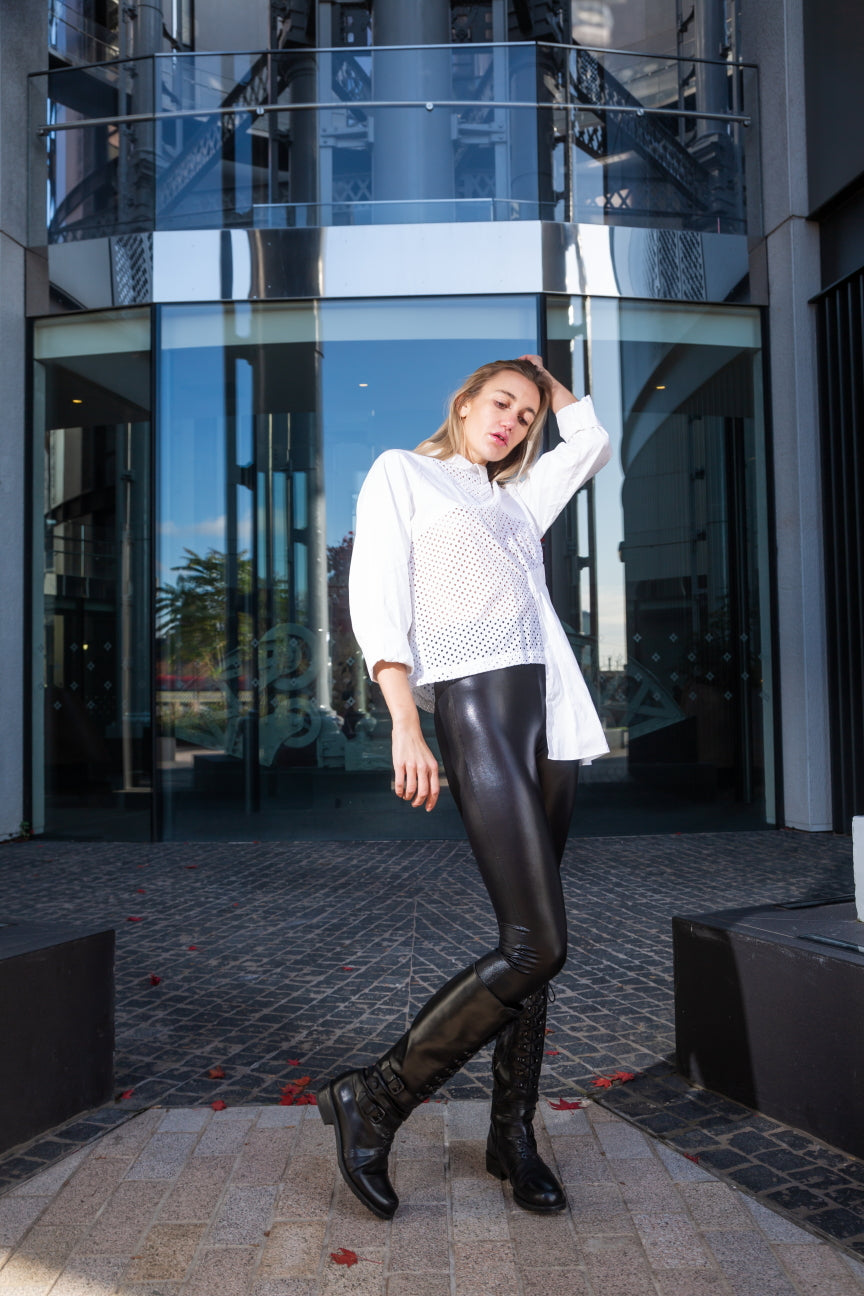 Woman in a white sweater and black leather pants standing in front of a modern building. White dotted blouse — handmade white designer blouse with delicate dot print from Major Minor Jakarta, relaxed fit, limited edition